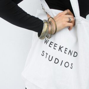 Stylish tote bag with 'Weekend Studios' text, worn casually with elegant bracelets.